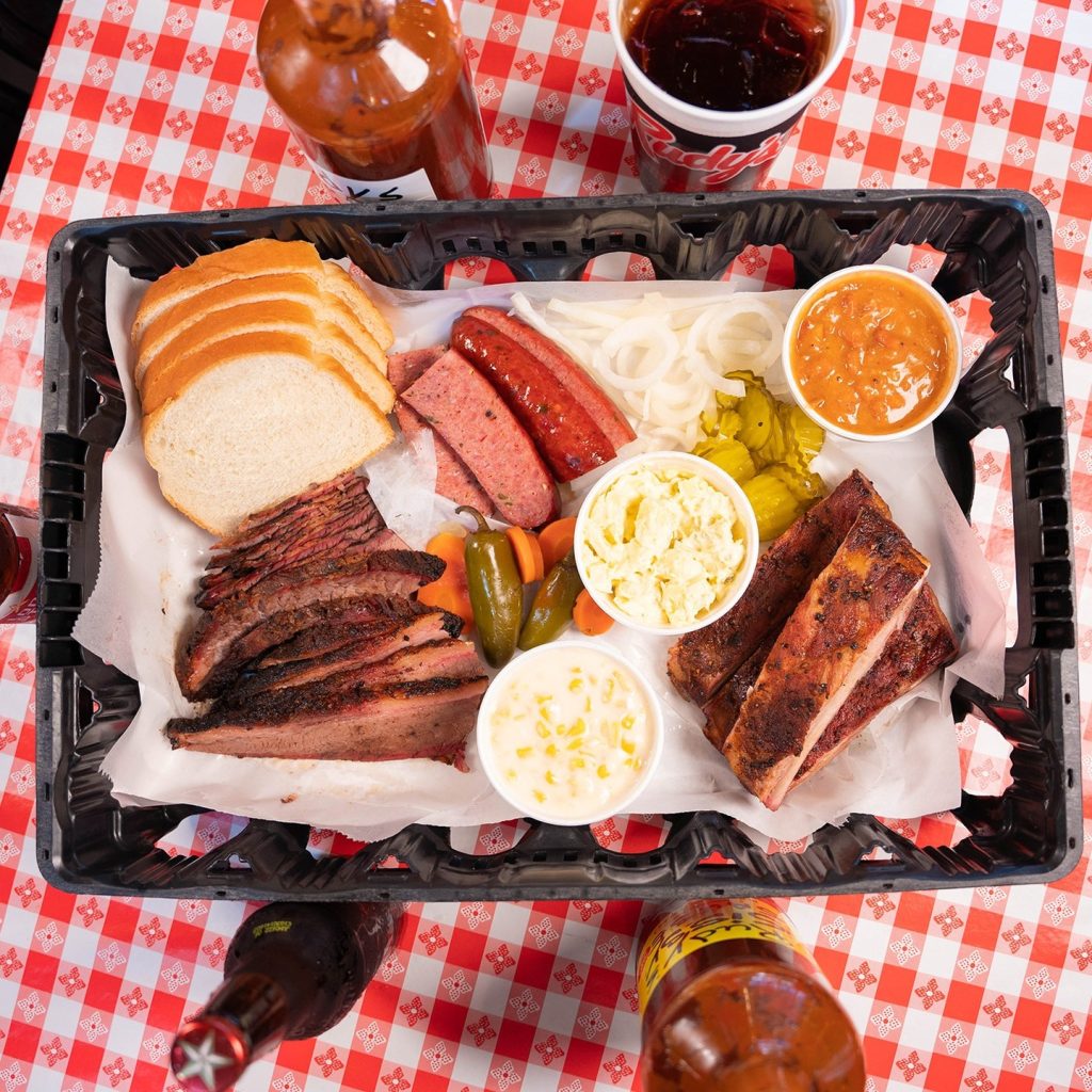 A group meal serving at Rudy’s, featuring various smoked meats and side dishes. Credit: @rudysbbq via Instagram