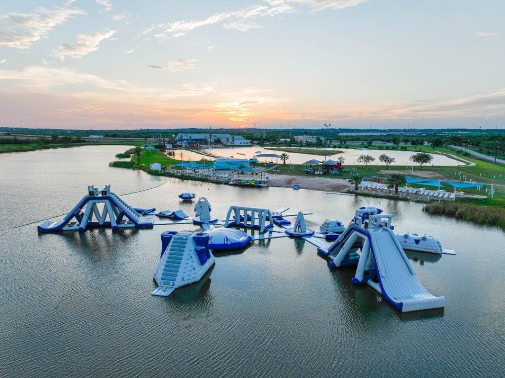 Aerial view of Texas Ski Ranch’s Aqua Park, a massive floating obstacle course that’s a summer favorite for all ages. Credit: @texasskiranch via Instagram