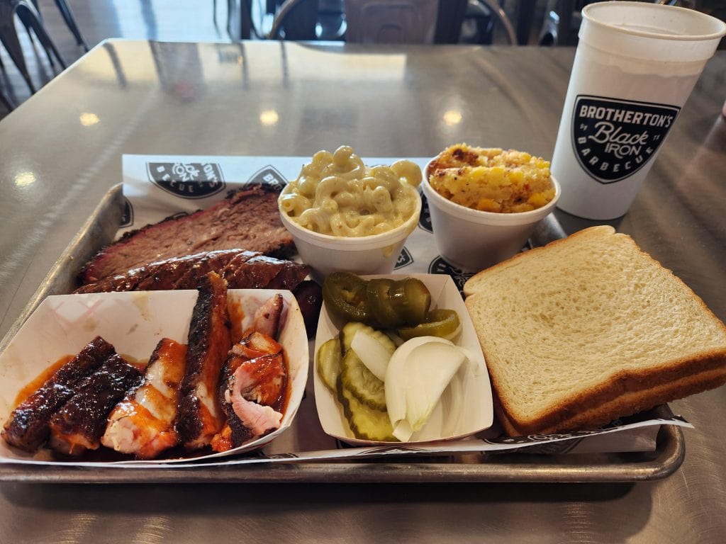 A hearty BBQ plate from Brotherton's Black Iron Barbecue with brisket, pork belly, chorizo, Oaxaca sausage, and classic sides. Credit: u/nanipenajr via r/BBQ