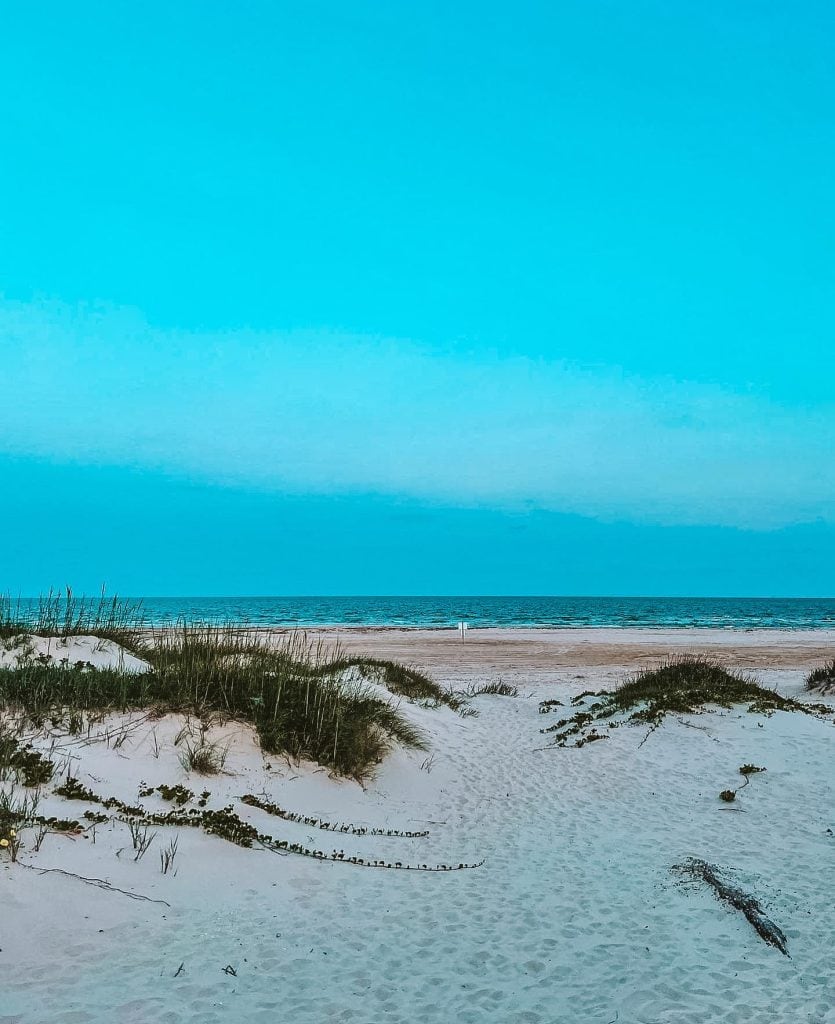 A scenic view of Matagorda Beach featuring striking blue water and soft, white sand stretching along the shore. Credit: @matagordabeach via Instagram