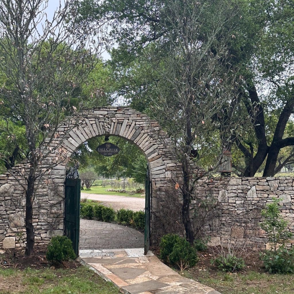 The welcoming entrance to Fall Creek Vineyards is lined with cobblestone fencing, tree-covered pathways, and peaceful nature views. Credit: @fallcreevineyards via Instagram