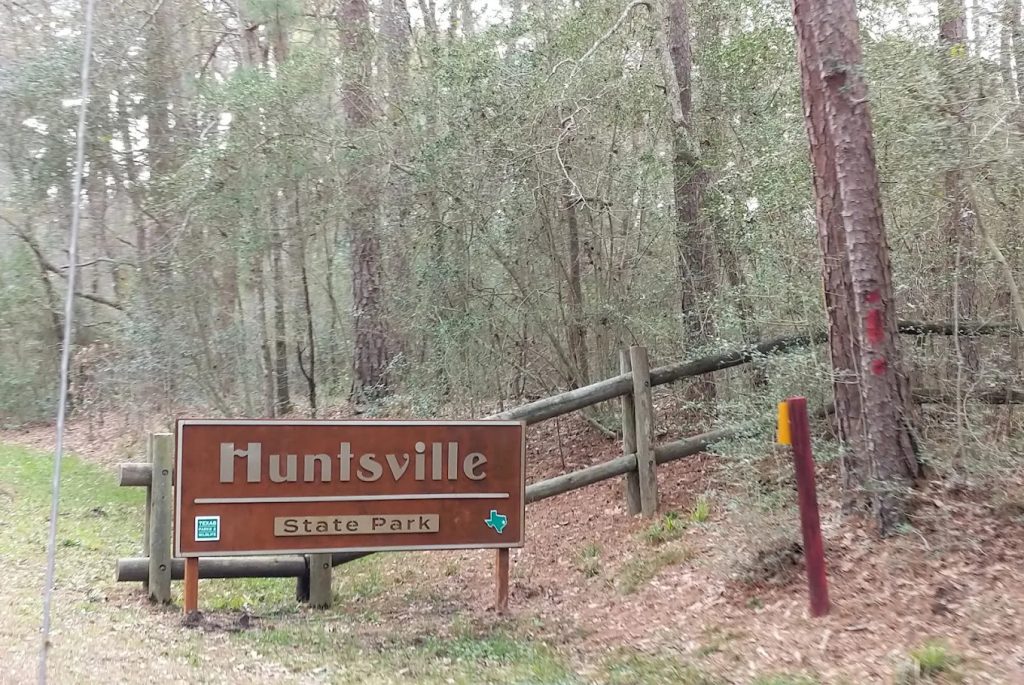 The Huntsville State Park sign stands tall with pine trees in the background, welcoming visitors to the Piney Woods. Credit: Maria Rosenberg