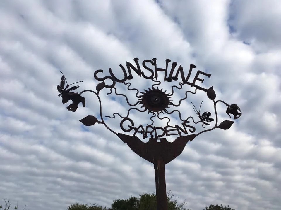 The Sunshine Gardens sign features butterflies, plants, and a sun symbol, reflecting the spirit of the space. Credit: Sunshine Community Gardens
