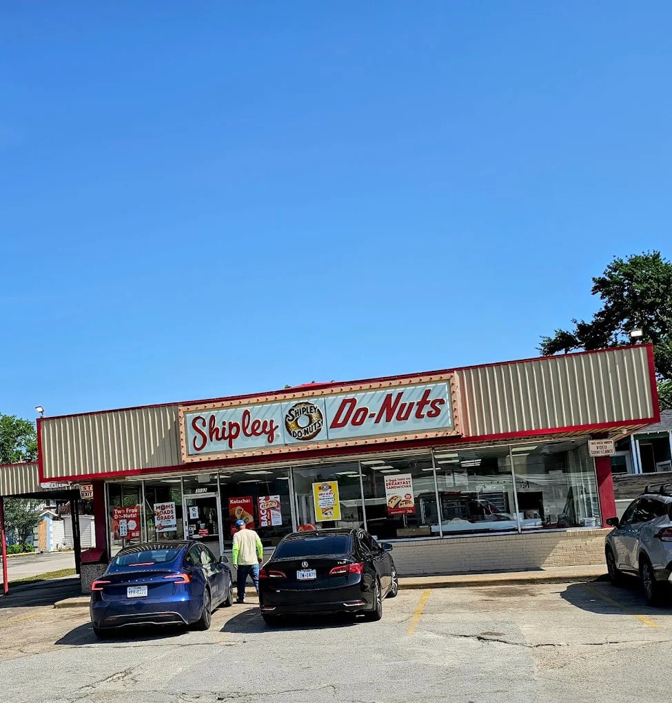 The façade of Shipley Do-Nuts is simple yet iconic, with red signage, their logo, and a glass storefront. Credit: un tal Plebe