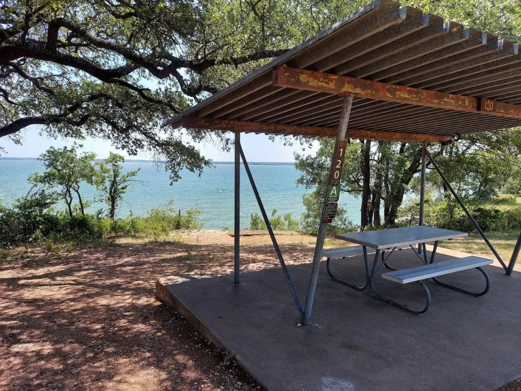 Picnic tables shaded by roofs overlook the lake, surrounded by trees for a peaceful family spot. Credit: Albert Tomchesson