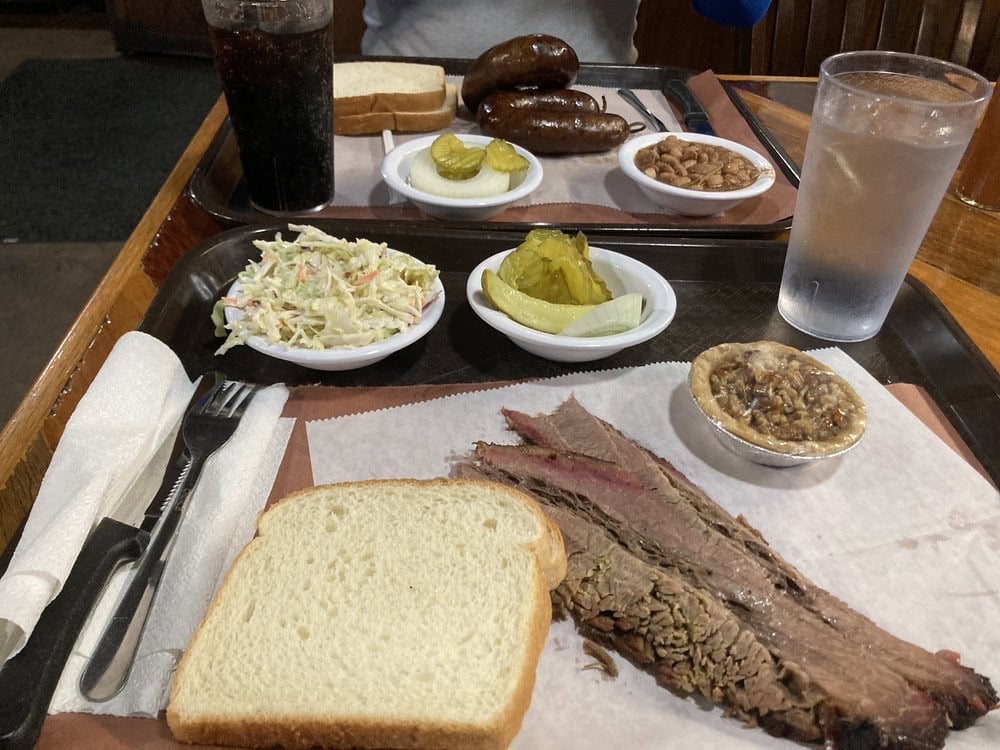 A full table spread includes meats, white bread, and sides like coleslaw, pickles, and baked beans. Credit: Hannah M.