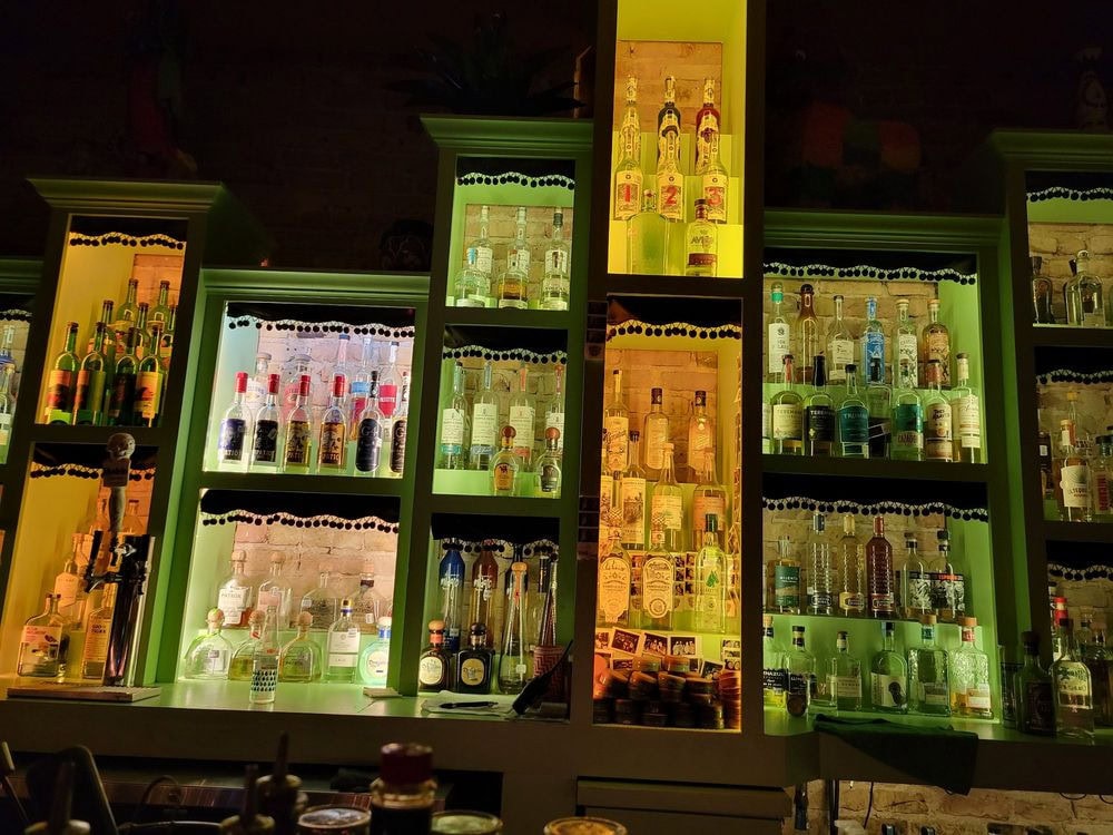 The tequila and mezcal bar glows with unique green lighting, highlighting hundreds of bottles on display. Credit: Nishma S.
