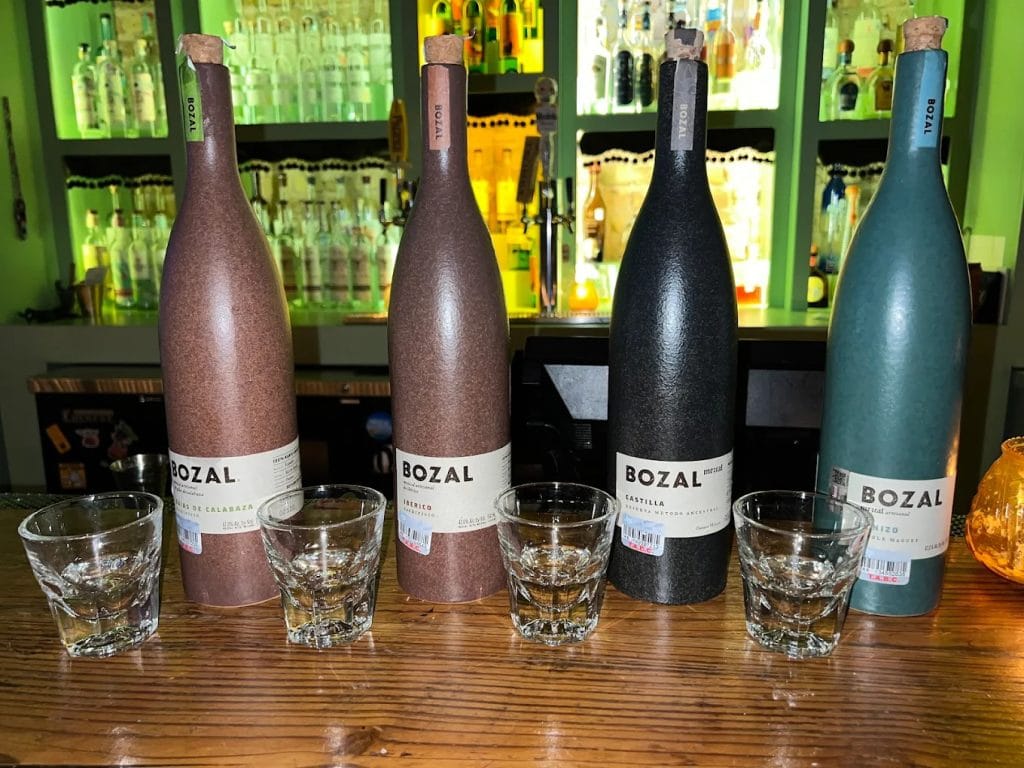 Four mezcal bottles are showcased with shots poured, just a glimpse of the endless varieties available. Credit: Bino Ad Astra Gopal