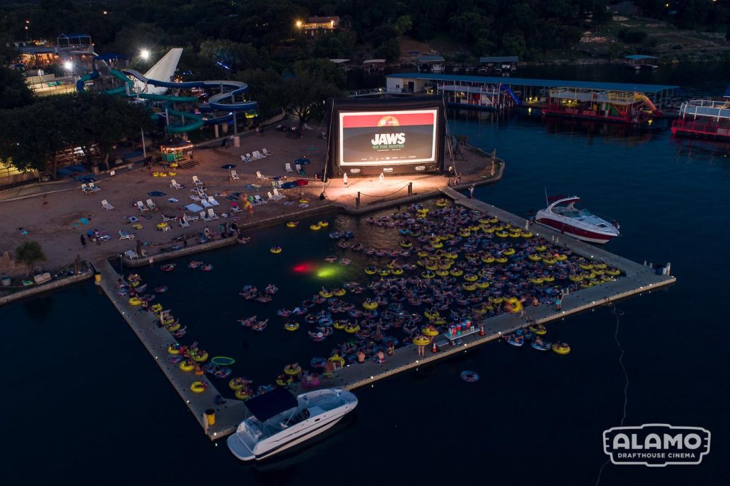 At night, Volente Beach hosts a Jaws screening where guests float on Lake Travis inside a makeshift pool—an unforgettable movie experience. Credit: u/SeasDiver