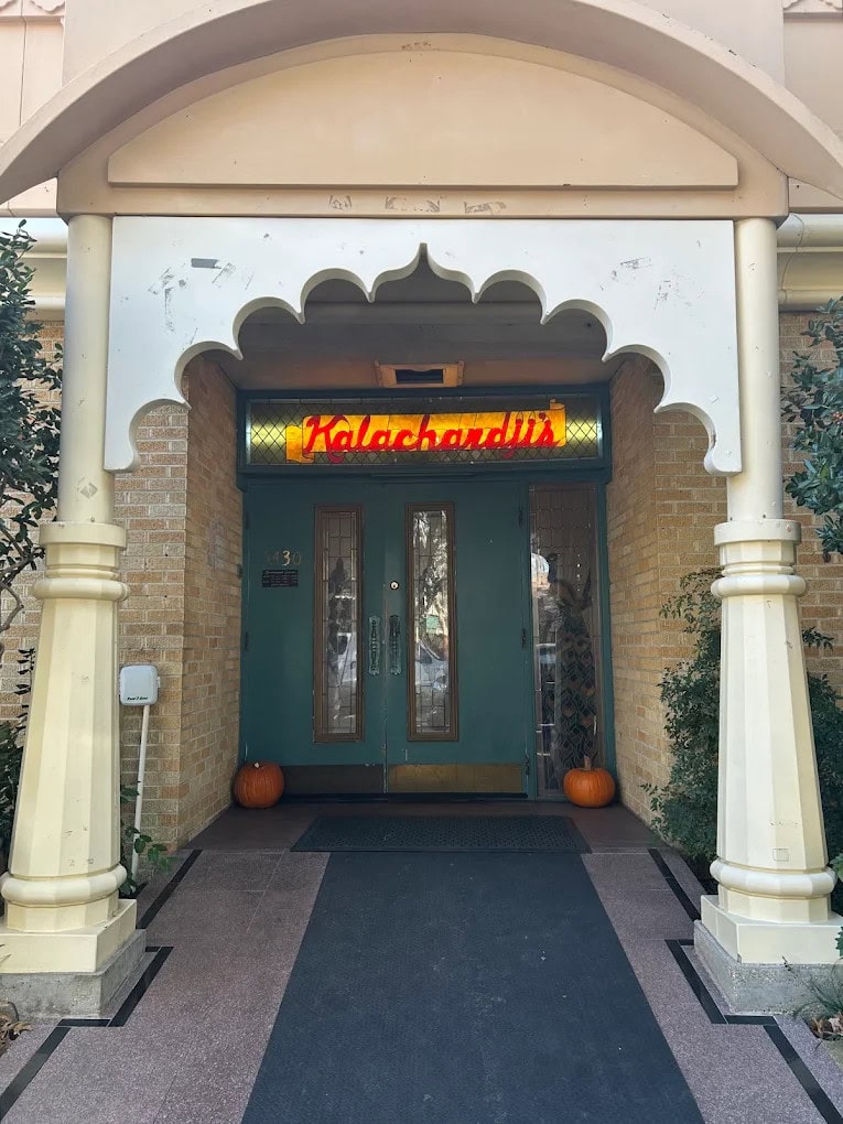 The façade of Kalachandji’s features Indian-inspired architecture, with a dark blue double-door entrance and a red-and-yellow sign. Credit: S B