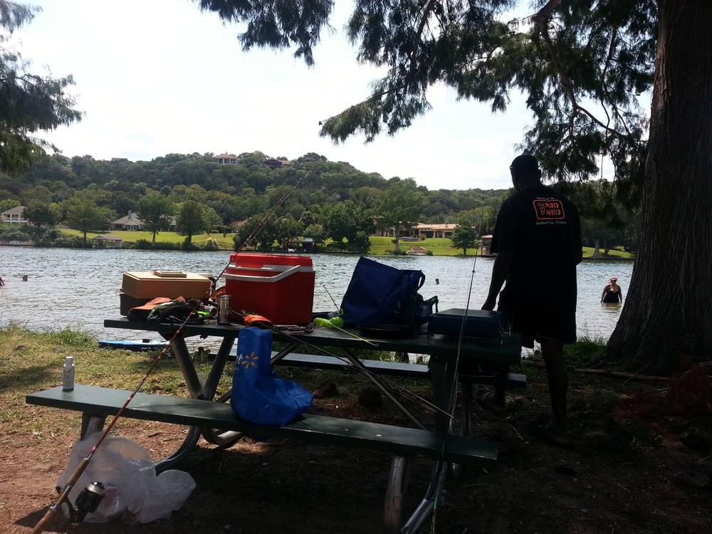 Families enjoy a lakeside feast at picnic tables filled with food and laughter. Credit: Leo C.