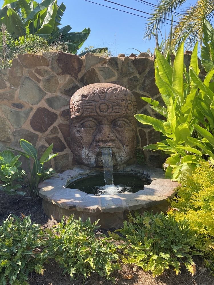 An exotic fountain shaped like an ancient figure pours water into a small pond, adding character to the space. Credit: Rina I.