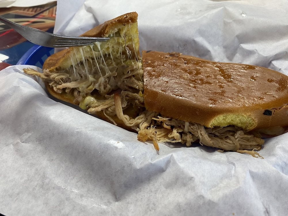 The medianoche sandwich combines roasted pulled pork, cheese, and sweet egg bread for a salty‑sweet delight. Credit: Tina D.