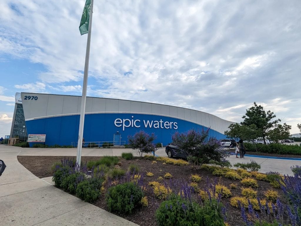 The entrance to Epic Waters Indoor Waterpark features a massive blue building with garden flowers and spacious parking. Credit: Andrew Anderson