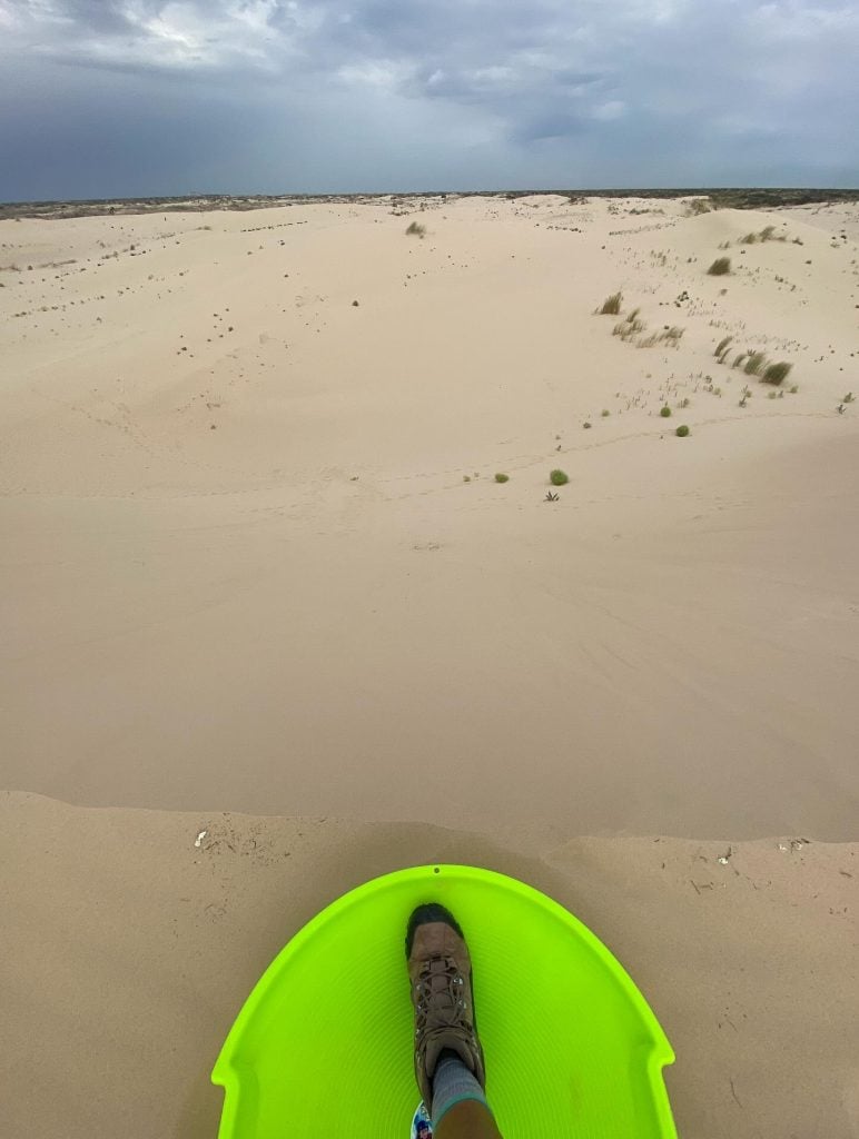 A POV shot moments before sand sledding down the dunes at Monahans Sandhills State Park—pure, simple fun. Credit: @texas_road_trips via Instagram