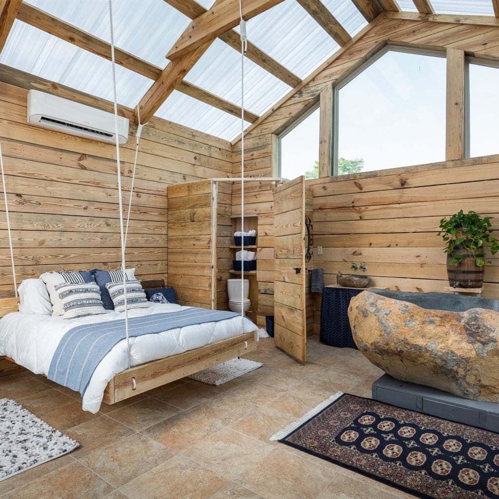 Inside one of the cabins, warm wooden interiors meet a calming white-and-blue palette, a hanging bed, and an earthenware soaking tub for a truly intimate retreat. Credit: @naturalistboudoir via Instagram