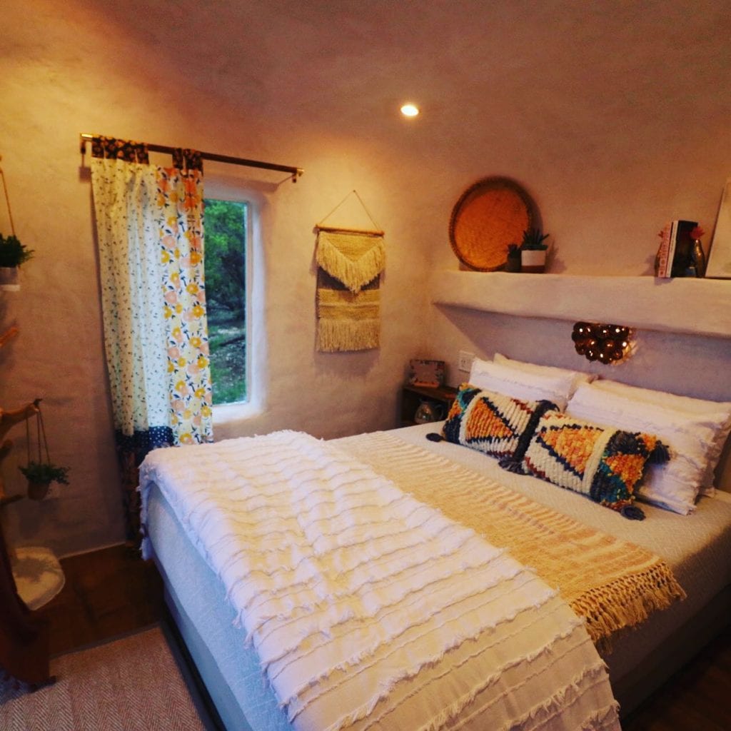 The bedroom at The Nest by Skybox Cabins features a calming boho design, soft white walls, and a large window framing stunning natural views. Credit: @skyboxcabins via Instaagram