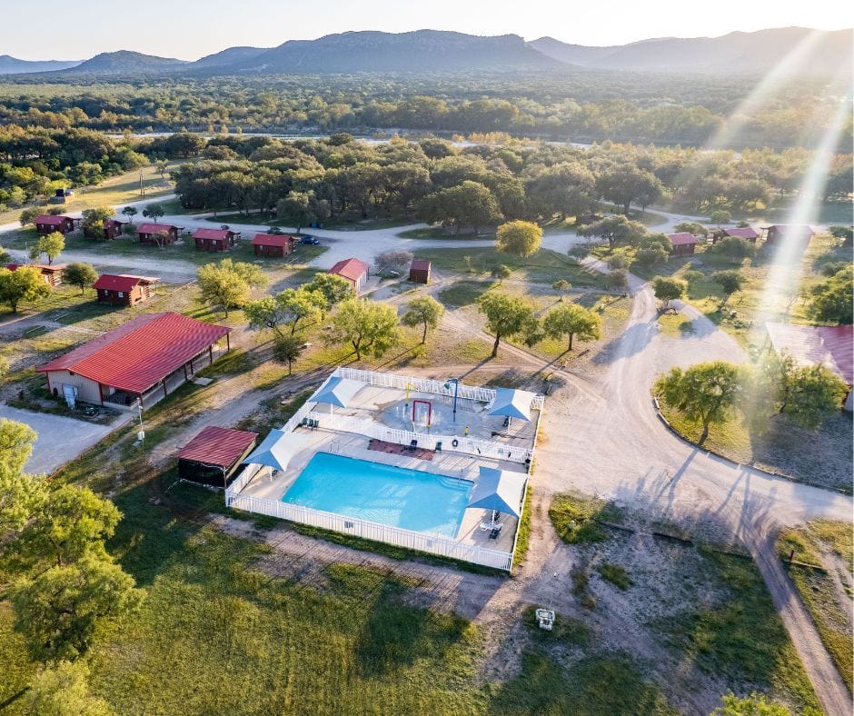 An aerial view of Nueces River RV & Cabin Resort, showcasing its expansive property with cabins, RV sites, and a swimming pool. Credit: @nuecesriverrv via Instagram