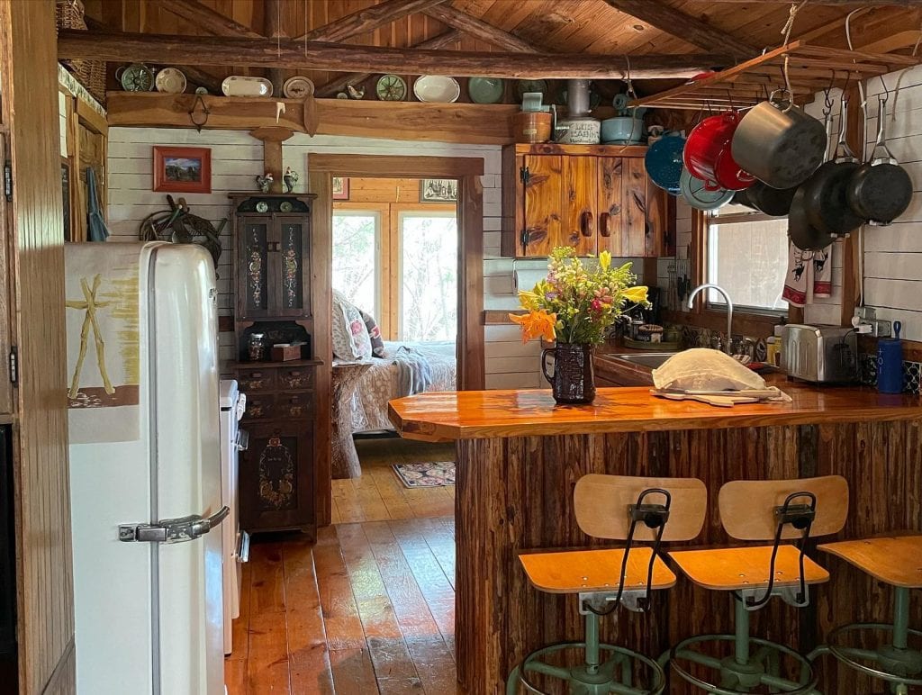 The cabin kitchen feels like stepping back into your grandparents’ home. Antique cookware, a vintage fridge, wooden interiors, and bar stools — warm, nostalgic, and inviting. Credit: @lake1290 via Instagram