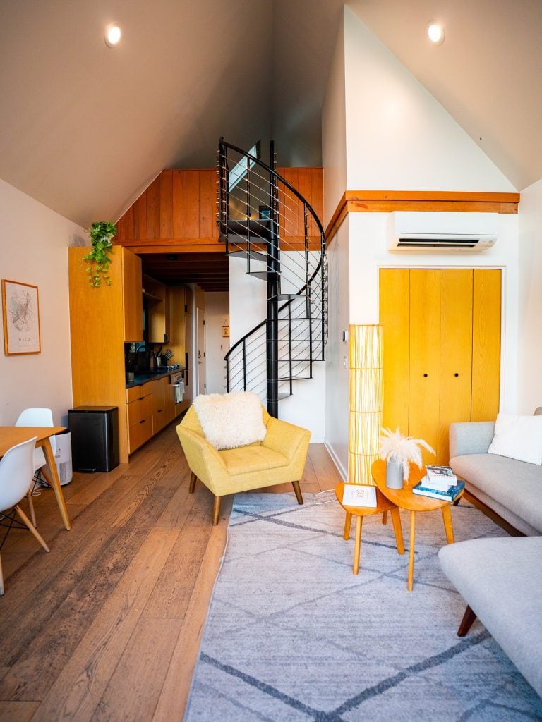 Inside Shadow Bend Cabin, a cozy minimalist interior features full amenities and a striking black spiral staircase leading to the loft bedroom. Credit: @liveoaklake via Instagram