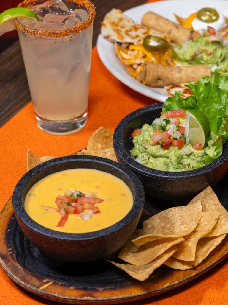 A classic Tex-Mex spread from El Fenix featuring queso, nachos, guacamole, quesadillas, and a refreshing cocktail rimmed with lime and Tajín. Credit: @elfenixmexican via Instagram