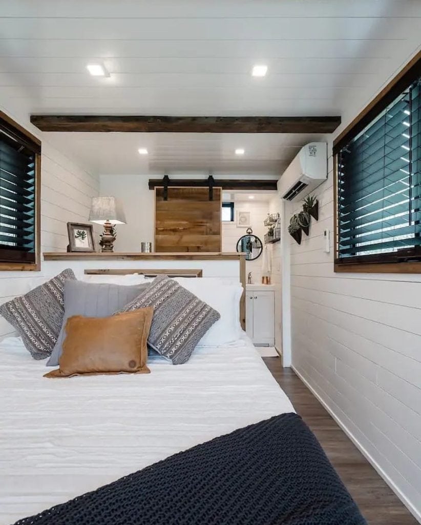 The first-floor bedroom at The Helm. Modern aesthetic softened with natural wood elements. Clean, uncluttered, and tucked in the back is the bathroom for added convenience. Credit: @tinyhouseperfect via Instagram