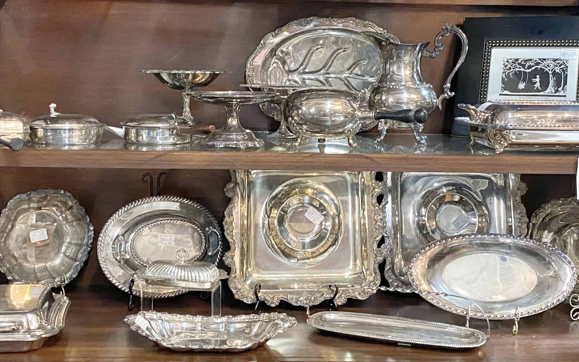 Shelf of vintage silver serving trays and pitchers at The Antique Gallery of Houston in Spring, Texas