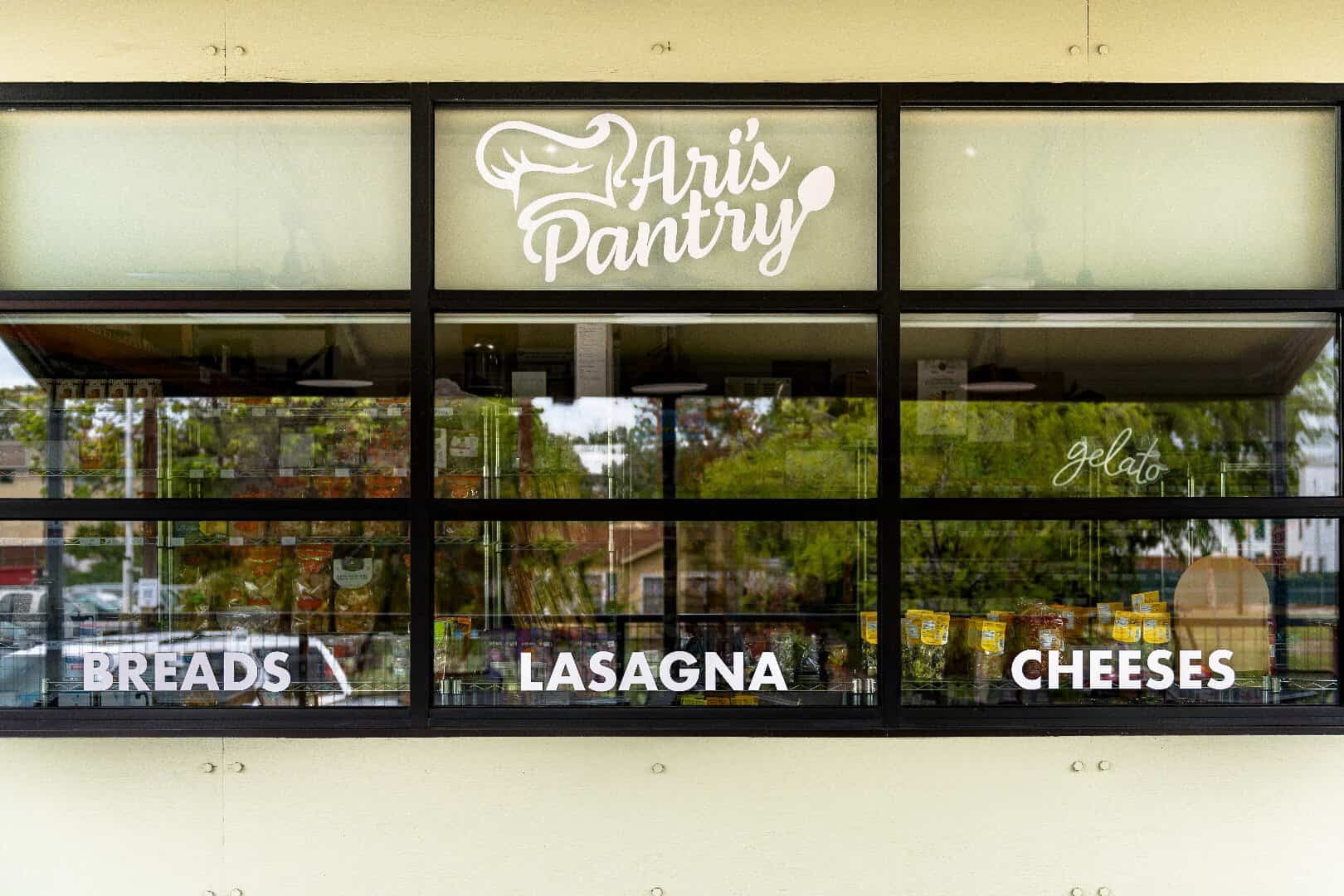 Storefront window signage at Ari's Pantry in Dallas reading breads, lasagna and cheeses