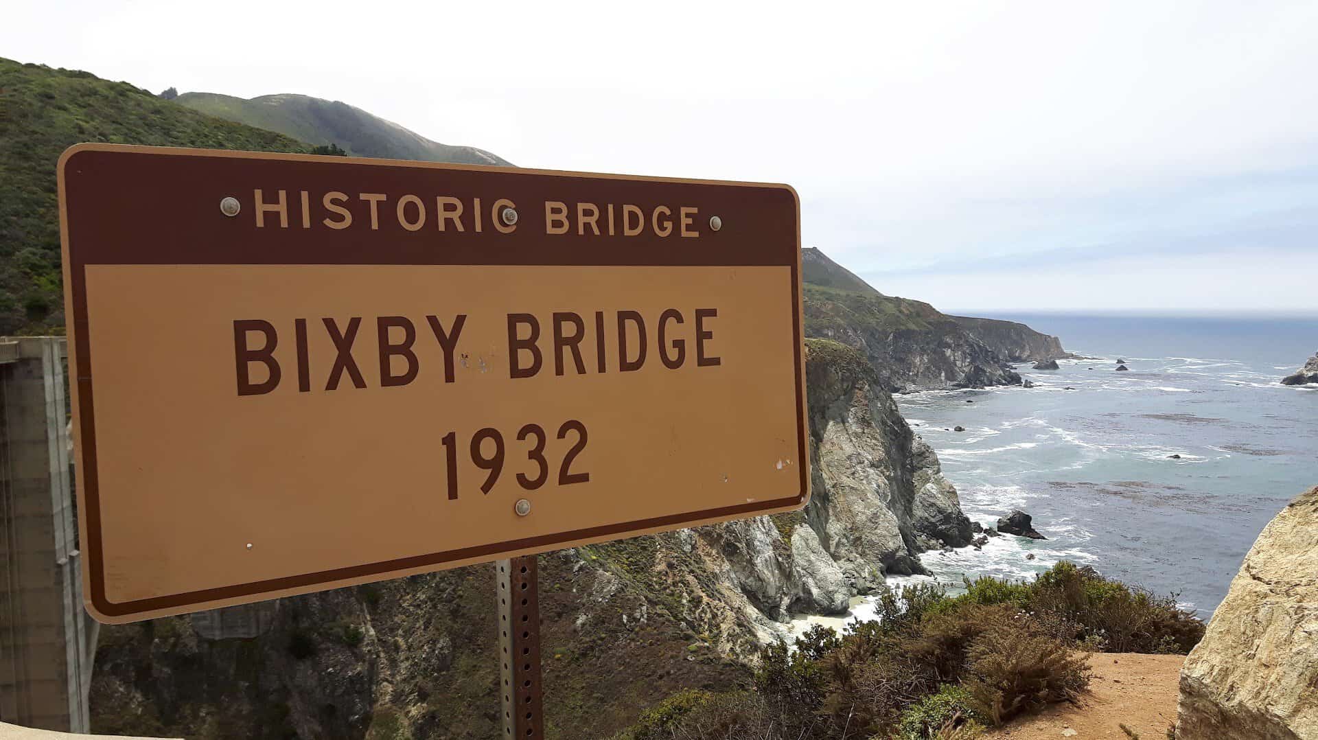 Historic Bixby Bridge marker with the Big Sur coastline and Pacific Ocean behind it, California
