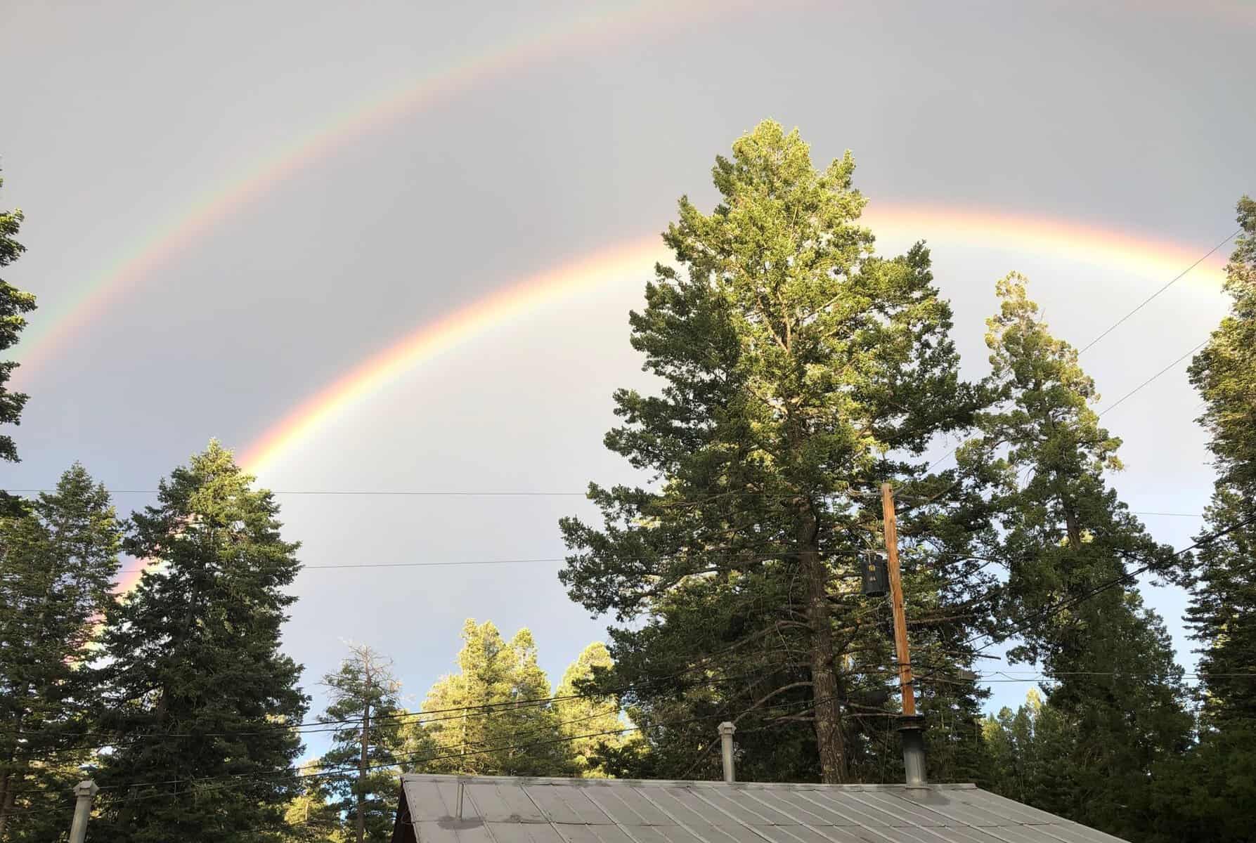 Mountain cabin deck under tall pines and a rainbow at The Cabins at Cloudcroft, New Mexico