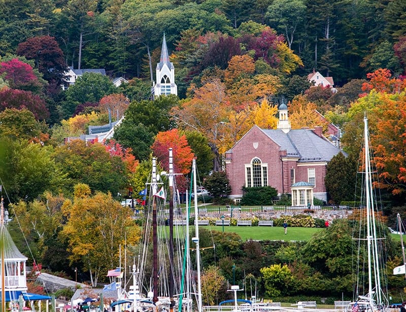 Camden Maine harbor with schooner masts, a brick church, and autumn foliage