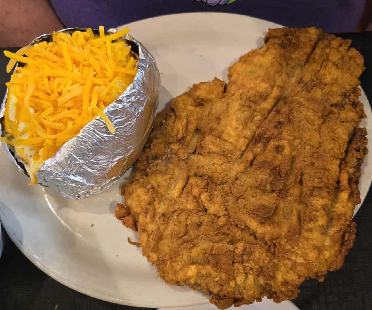 Large chicken fried steak served with a cheese-topped baked potato at Hofbrau Steaks in Porter, Texas