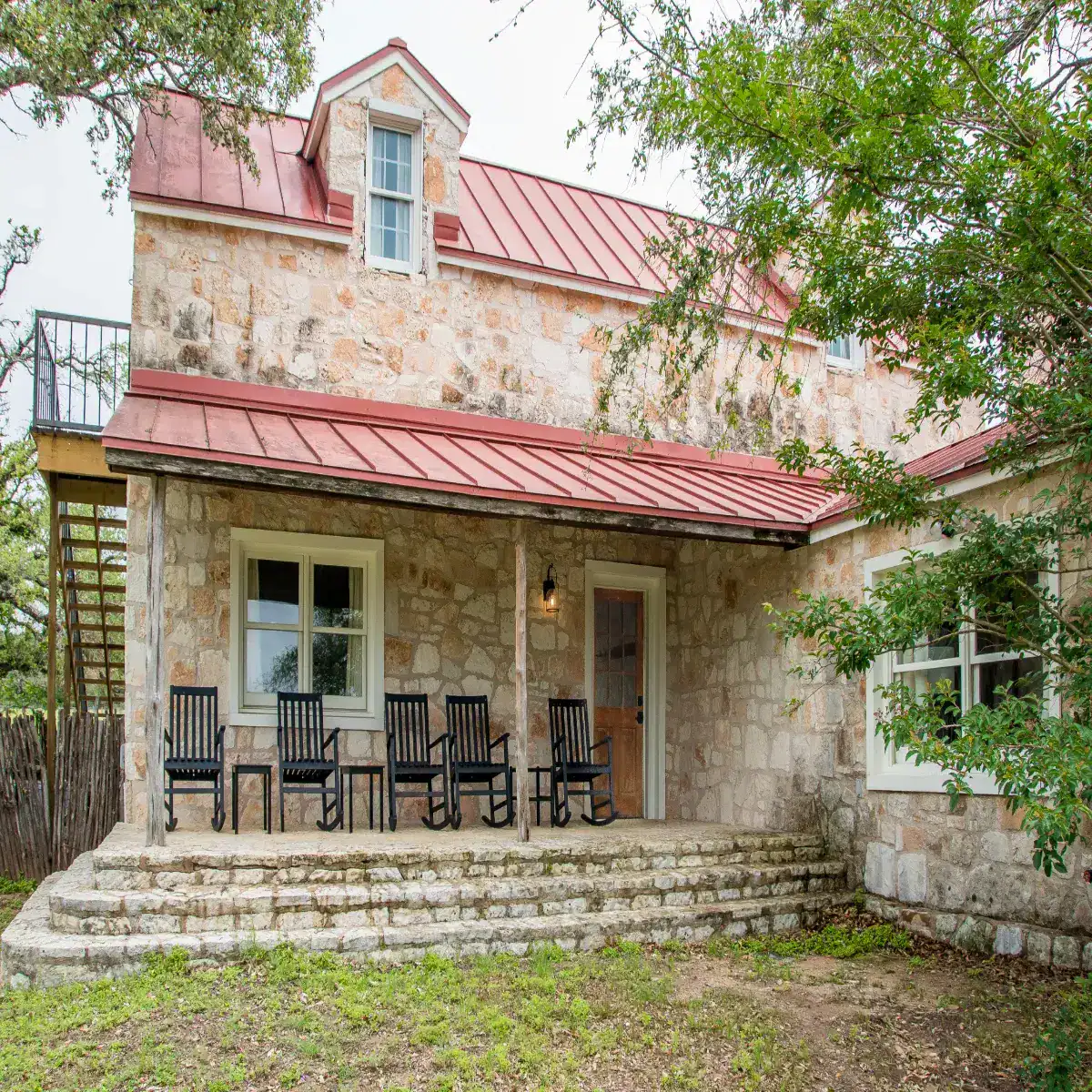 Restored 1800s stone log cabin with a rocking-chair porch at Contigo Ranch in Fredericksburg, Texas