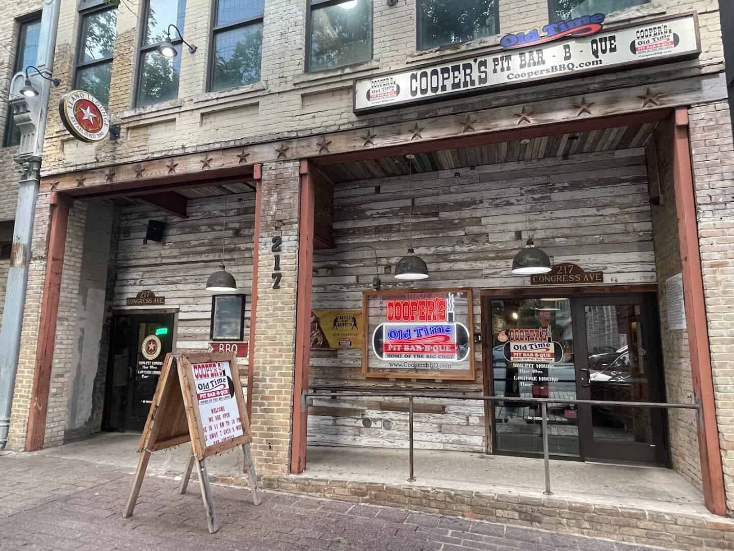 Weathered wood storefront of Cooper's Old Time Pit Bar-B-Que on Congress Avenue in downtown Austin