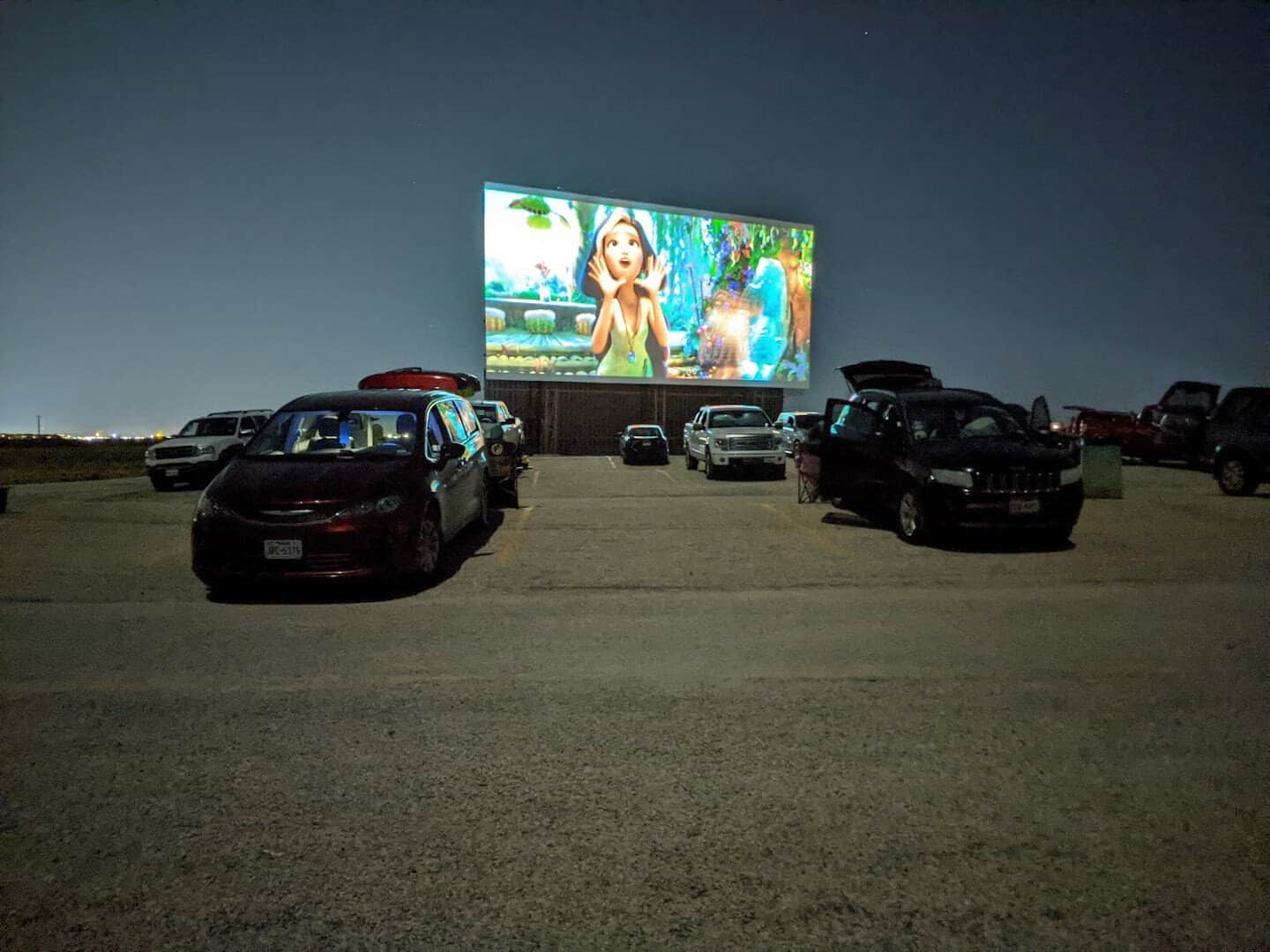 Row of cars facing the glowing screen at night at the New Braunfels drive-in