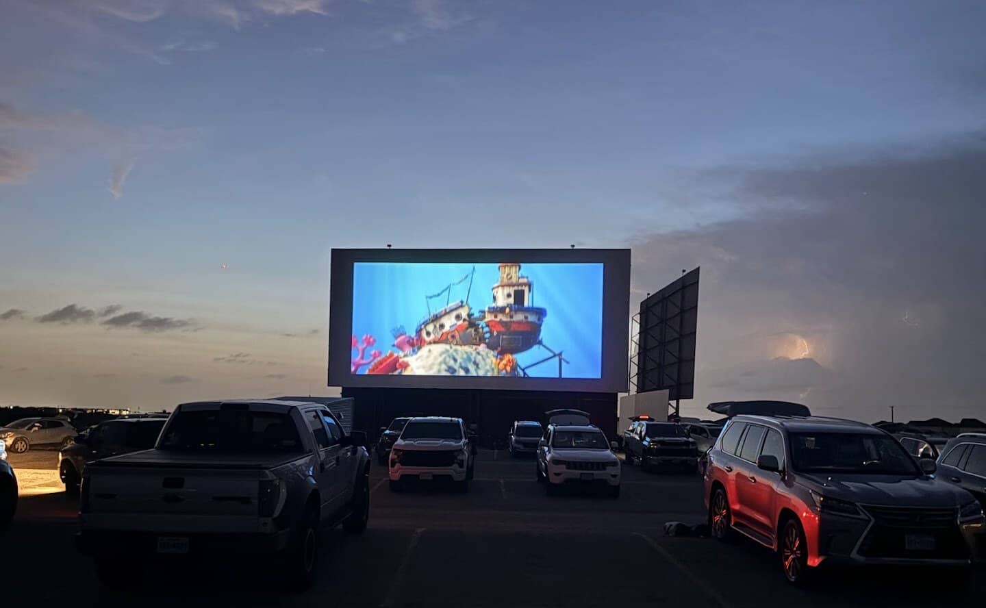 Cars watching a lit drive-in screen at night in New Braunfels, Texas