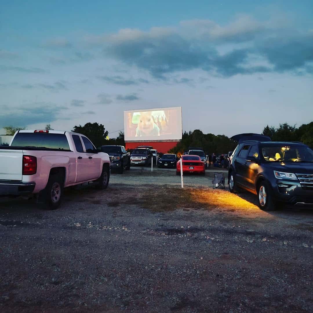 Cars parked in the gravel lot at dusk as a movie plays on the screen at The Last Drive-In Picture Show in Gatesville, Texas