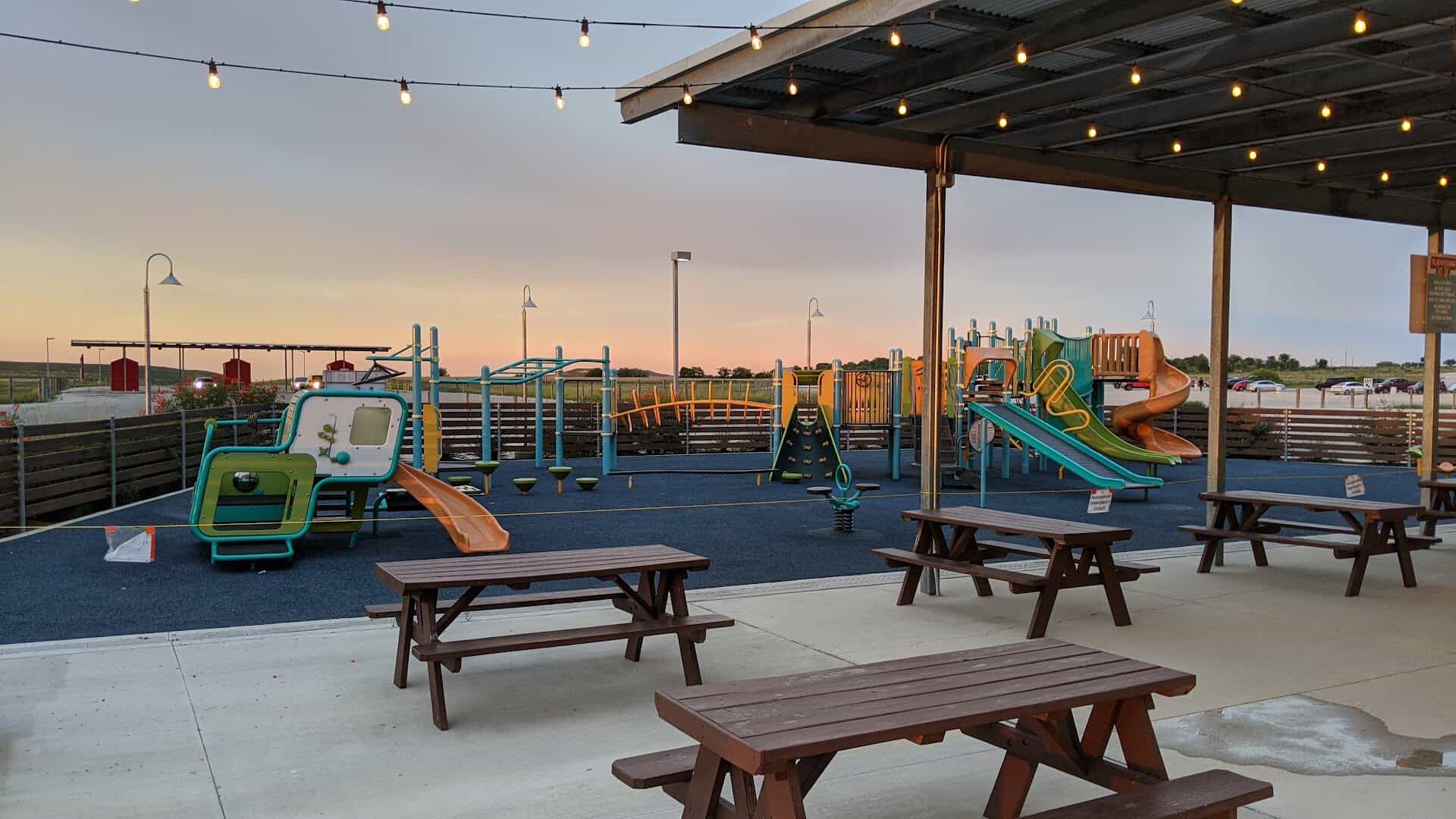 Playground and covered picnic tables with string lights at the New Braunfels drive-in