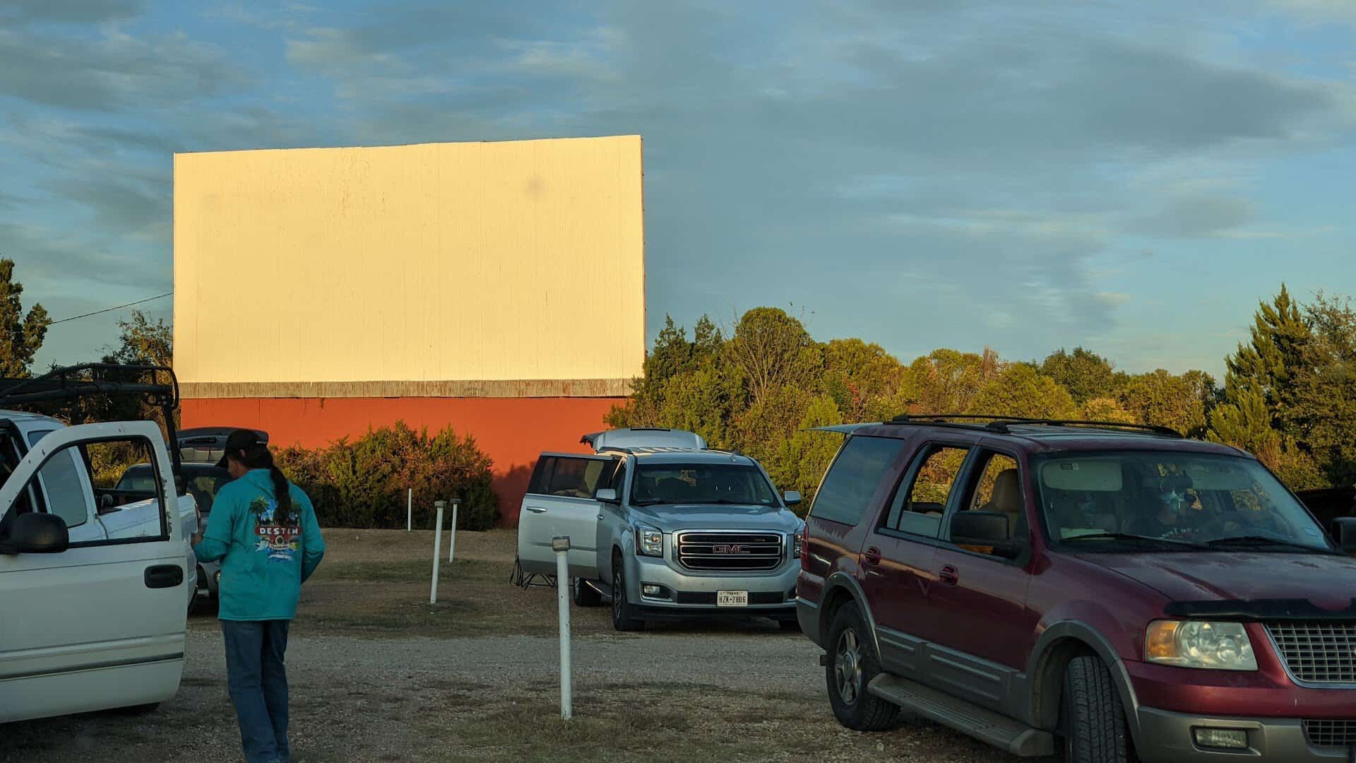 The drive-in screen glowing at golden hour with cars gathered in the lot at The Last Drive-In Picture Show in Gatesville, Texas