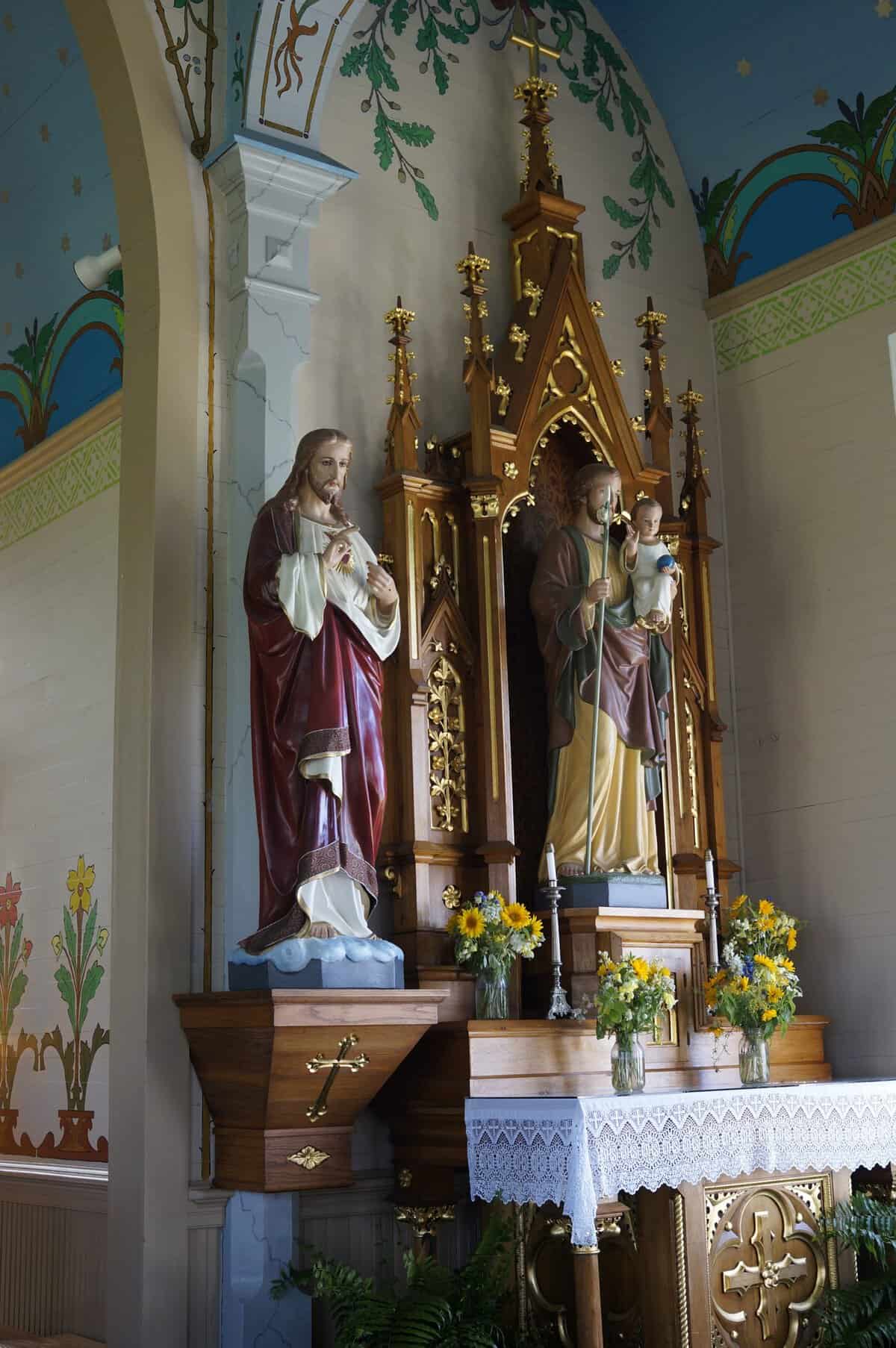 Sacred Heart and Saint Joseph statues on a side altar with painted floral walls in Dubina, Texas