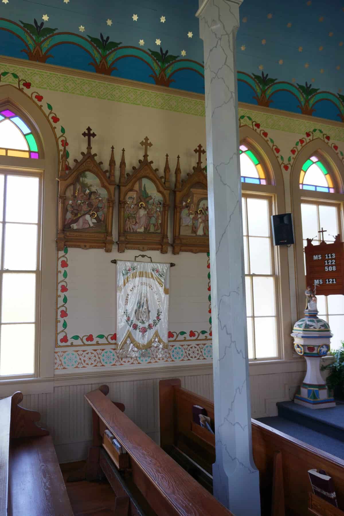Painted nave with stained glass windows and a baptismal font inside a historic church in Dubina, Texas