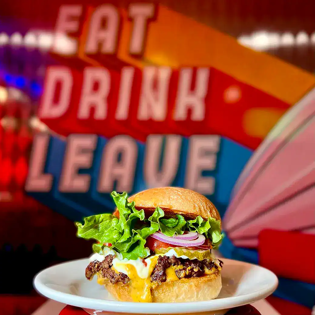 Cheeseburger below the EAT DRINK LEAVE neon sign at Ed Debevic's in Chicago, Illinois