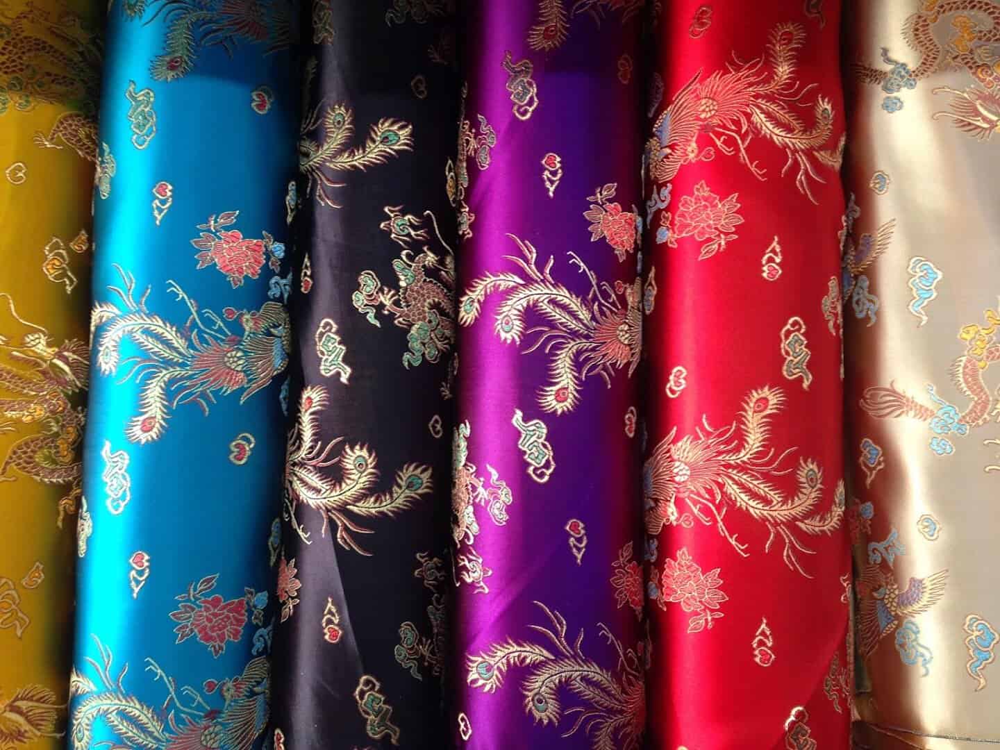 Colorful brocade fabric bolts in teal, pink, red and gold at Fabrictopia in Houston