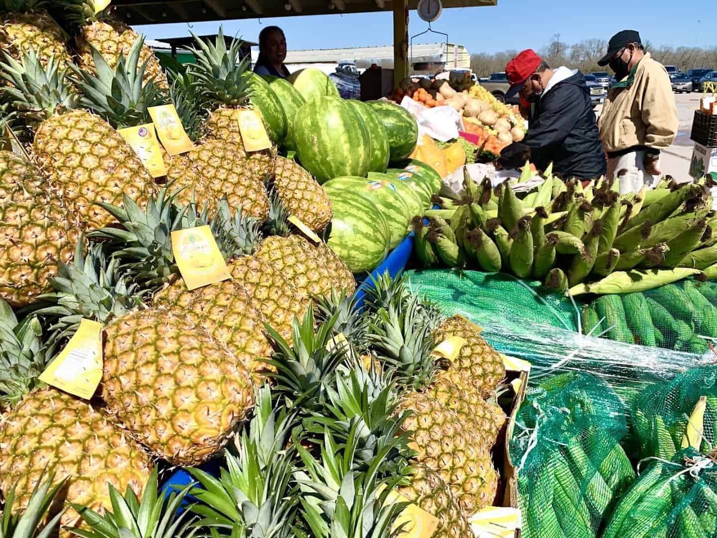 Pineapples, watermelons and plantains piled on a produce table at Cole's flea market in Pearland, Texas