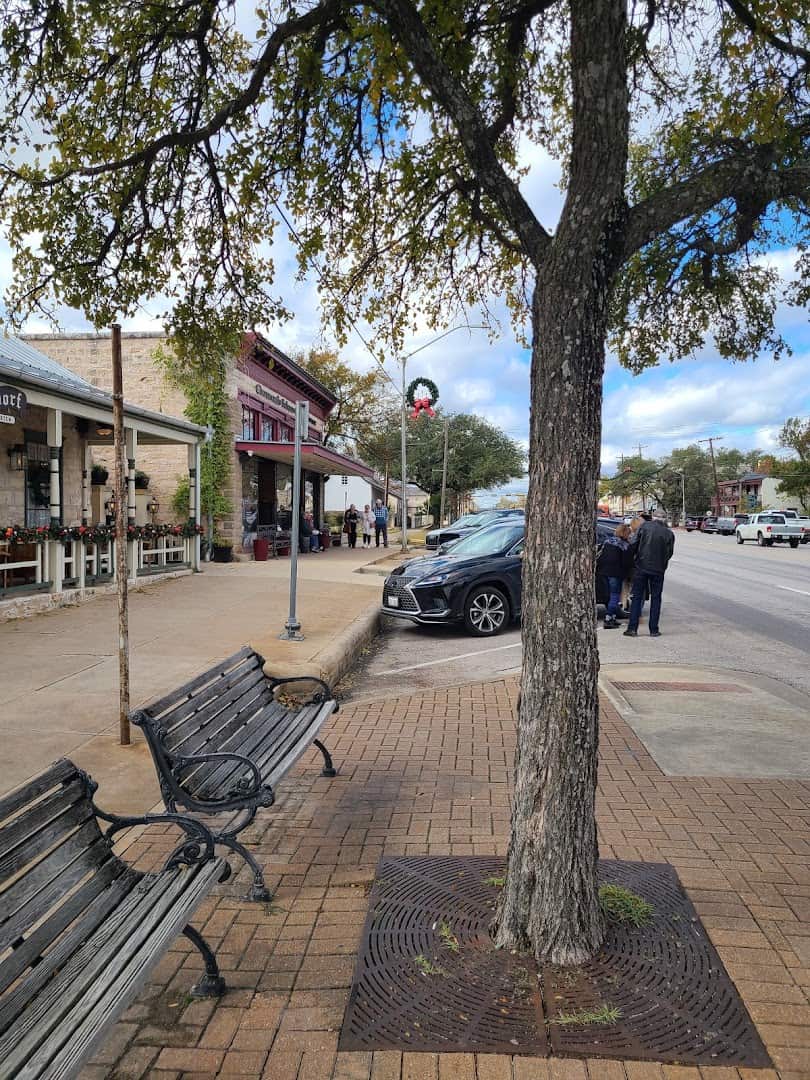 Tree-lined Main Street with a bench and storefronts in Fredericksburg, Texas