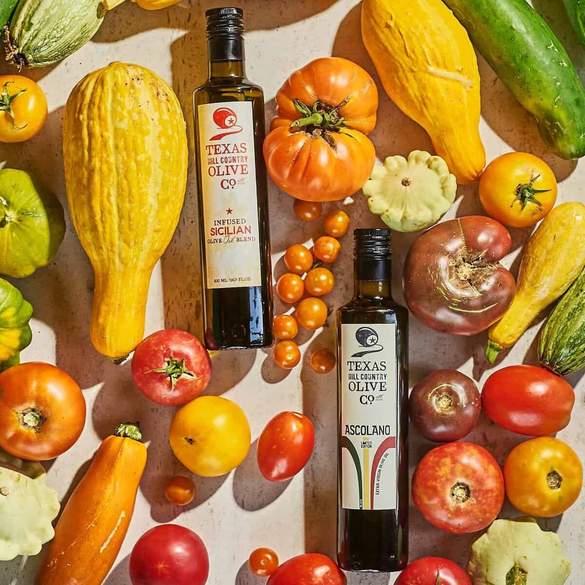 Texas Hill Country Olive Co. extra virgin olive oil bottles among fresh tomatoes and squash