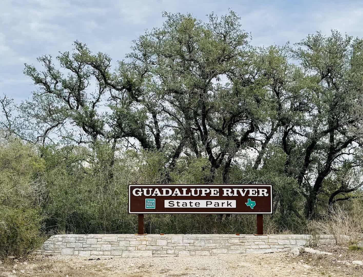The Guadalupe River State Park entrance sign beneath a live oak in Spring Branch, Texas