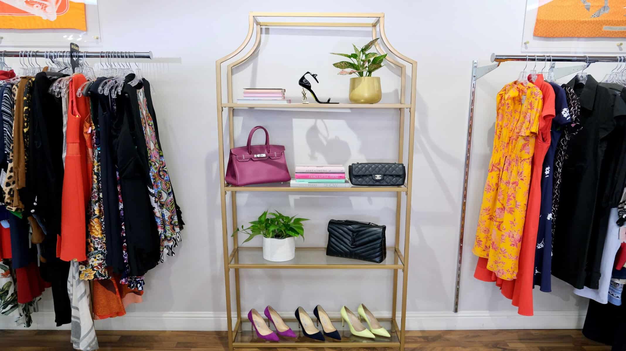 A display shelf of handbags and shoes beside clothing racks at Clotheshorse Anonymous in Dallas