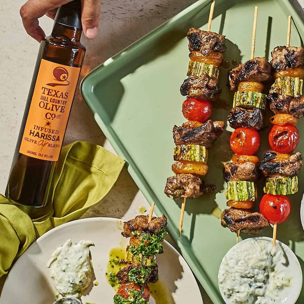 Texas Hill Country harissa infused olive oil beside grilled vegetable and beef kebabs