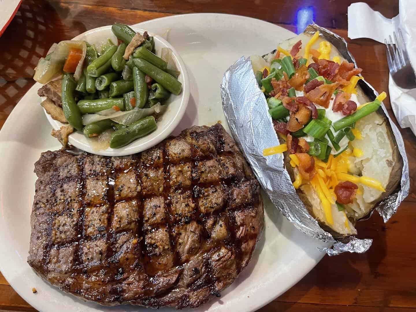 Grilled ribeye with a loaded baked potato and green beans at Hofbrau Steaks in Porter, Texas